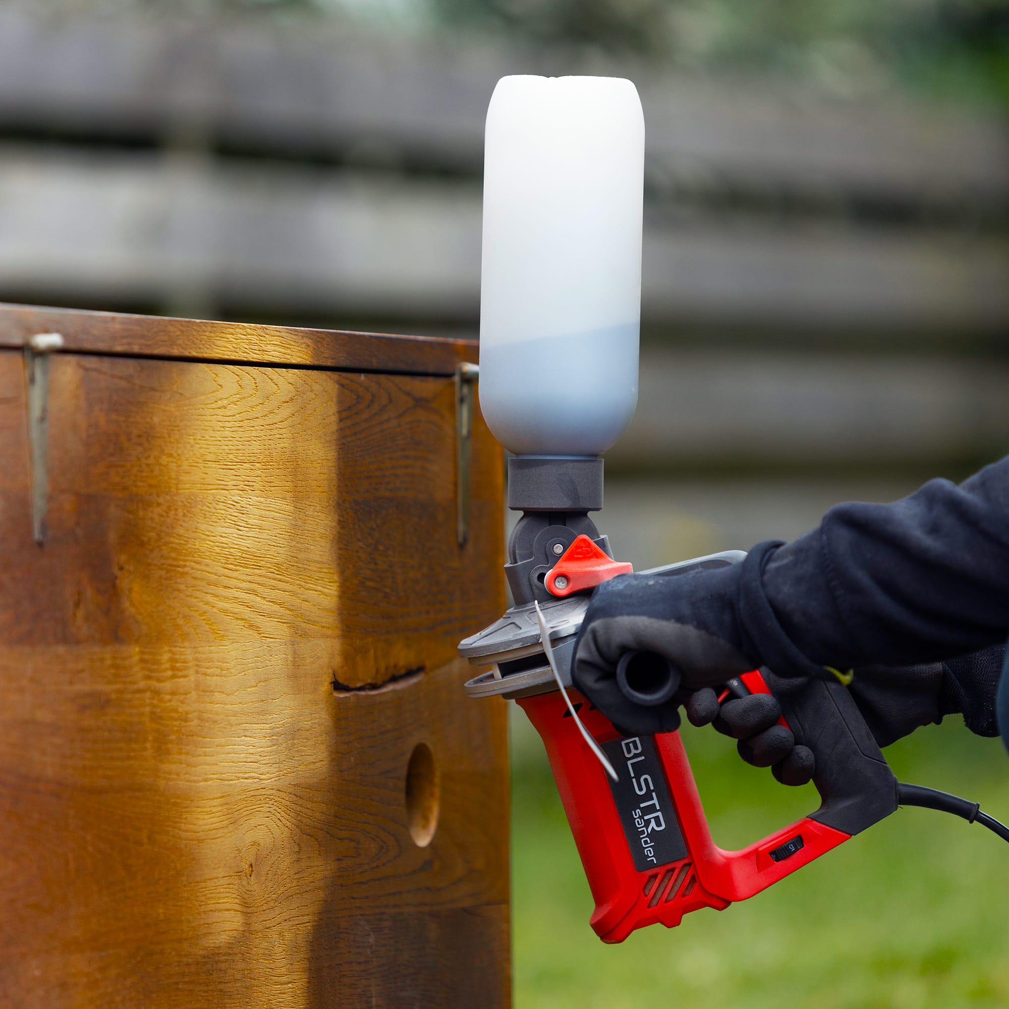 A gloved hand using the BLSTR sander on a varnished wooden barrel outdoors